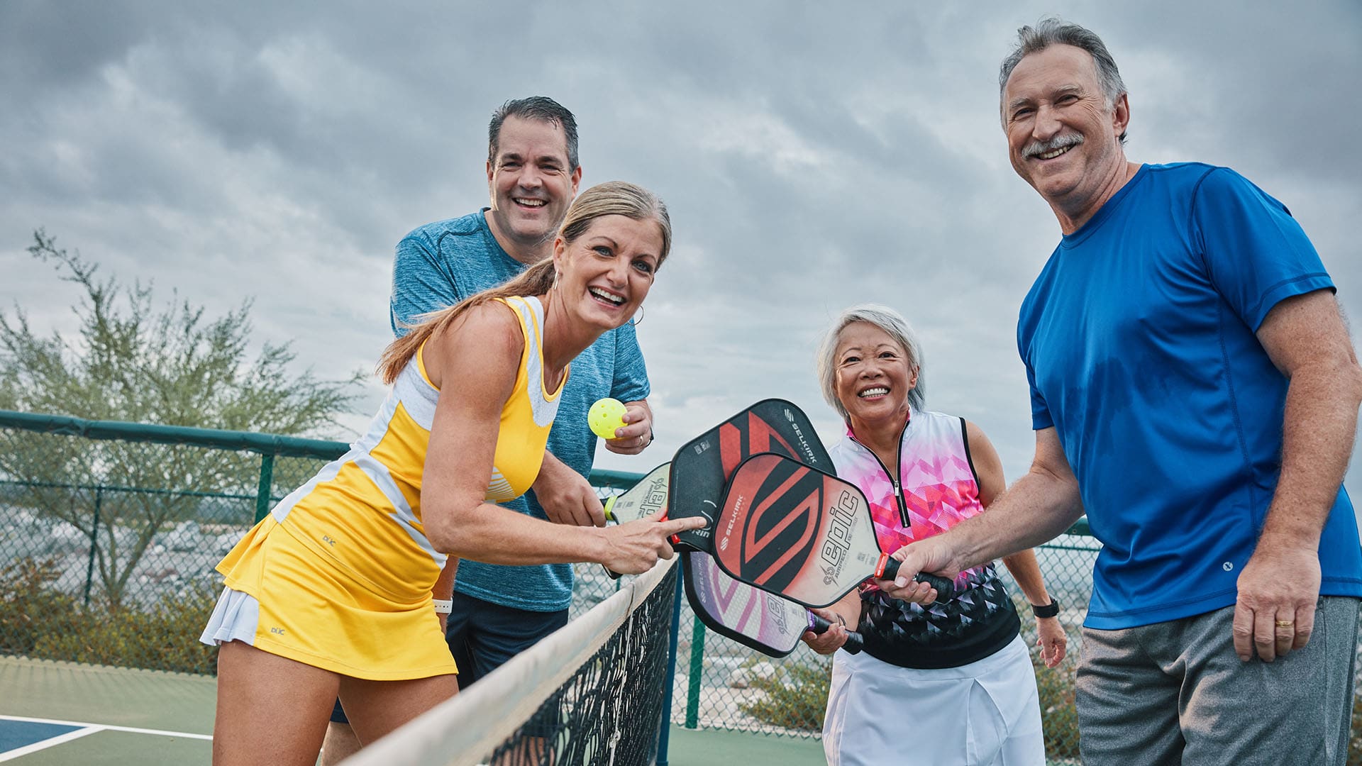 Two couples pose for a photo on a tennis court.