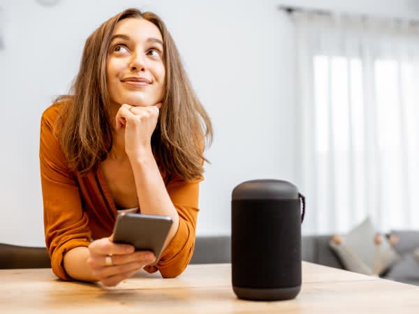 Woman smiling holding a smartphone next to a bluetooth speaker