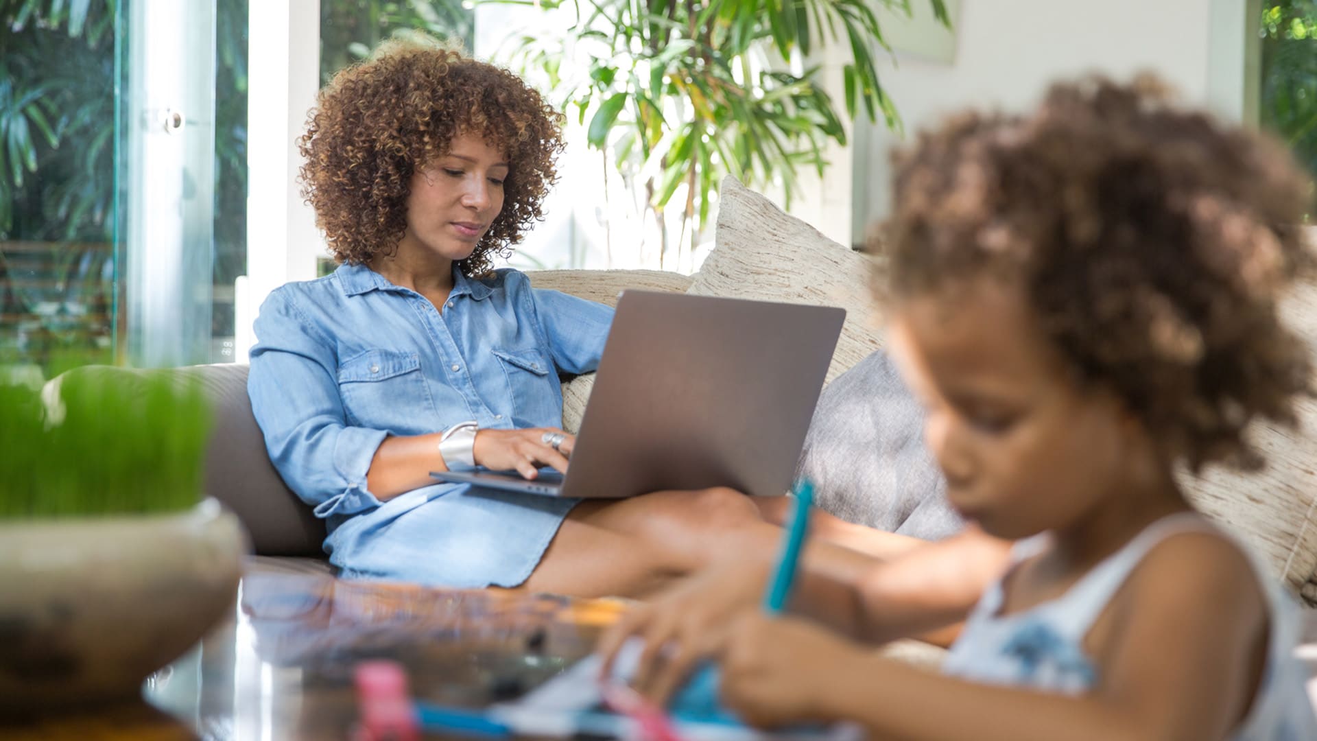 mother using laptop on couch while young daughter is coloring